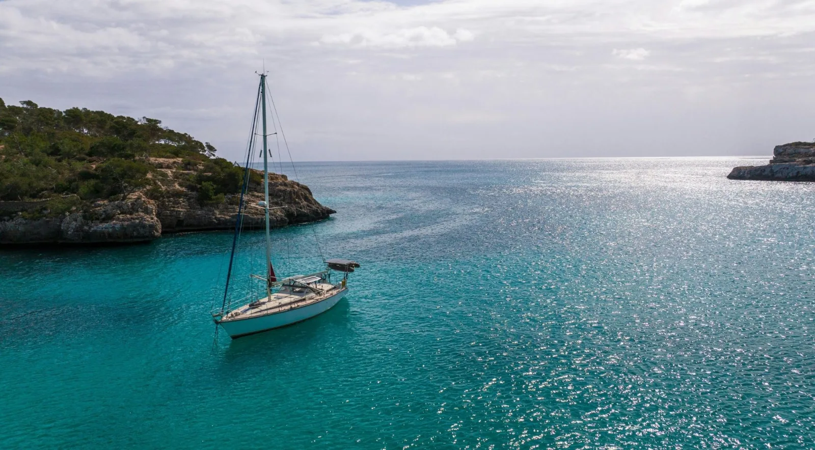 A single sailing yacht anchored in a calm Mallorcan cove in morning light