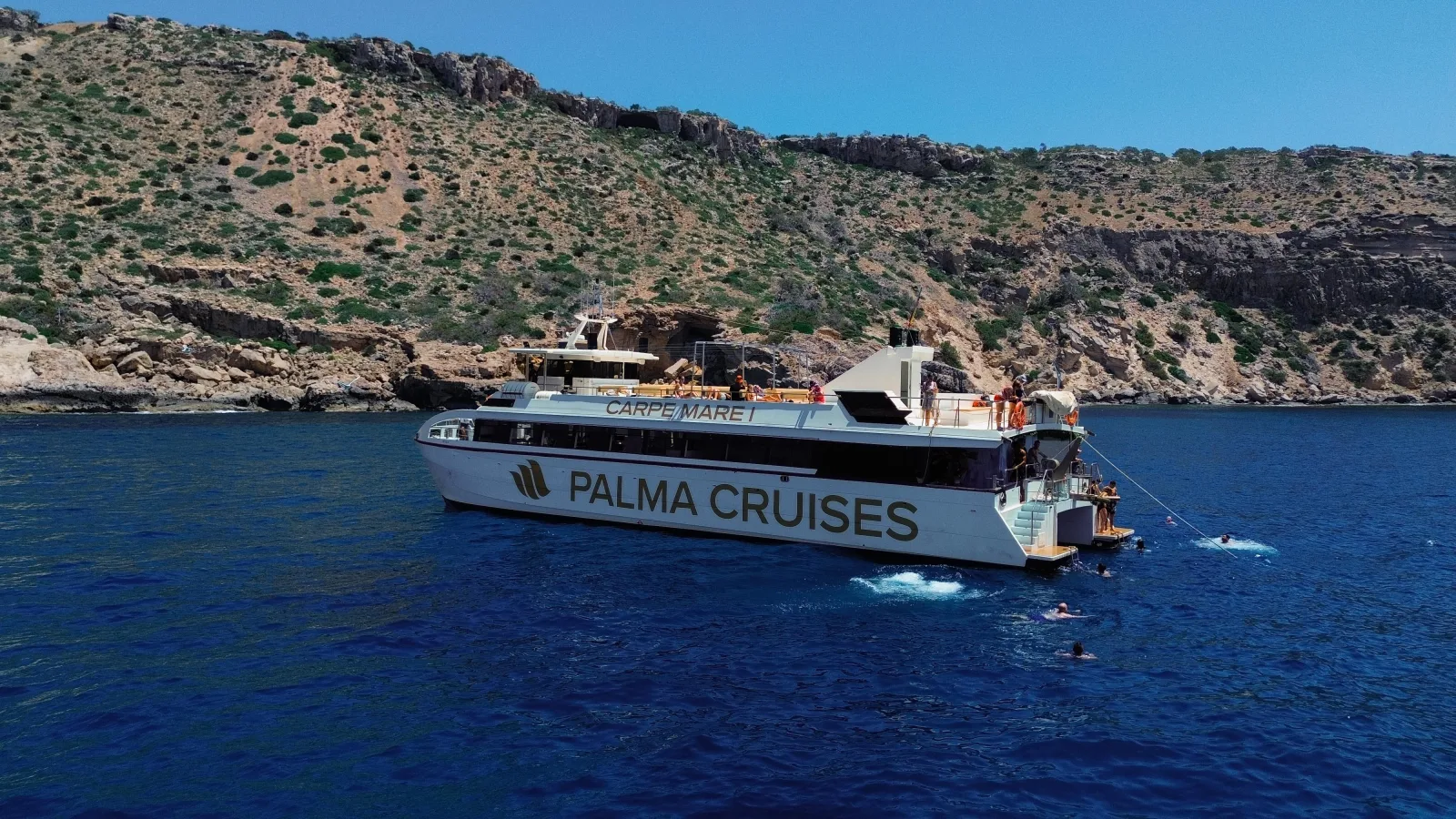 The Palma Cruises boat moored below a rocky headland